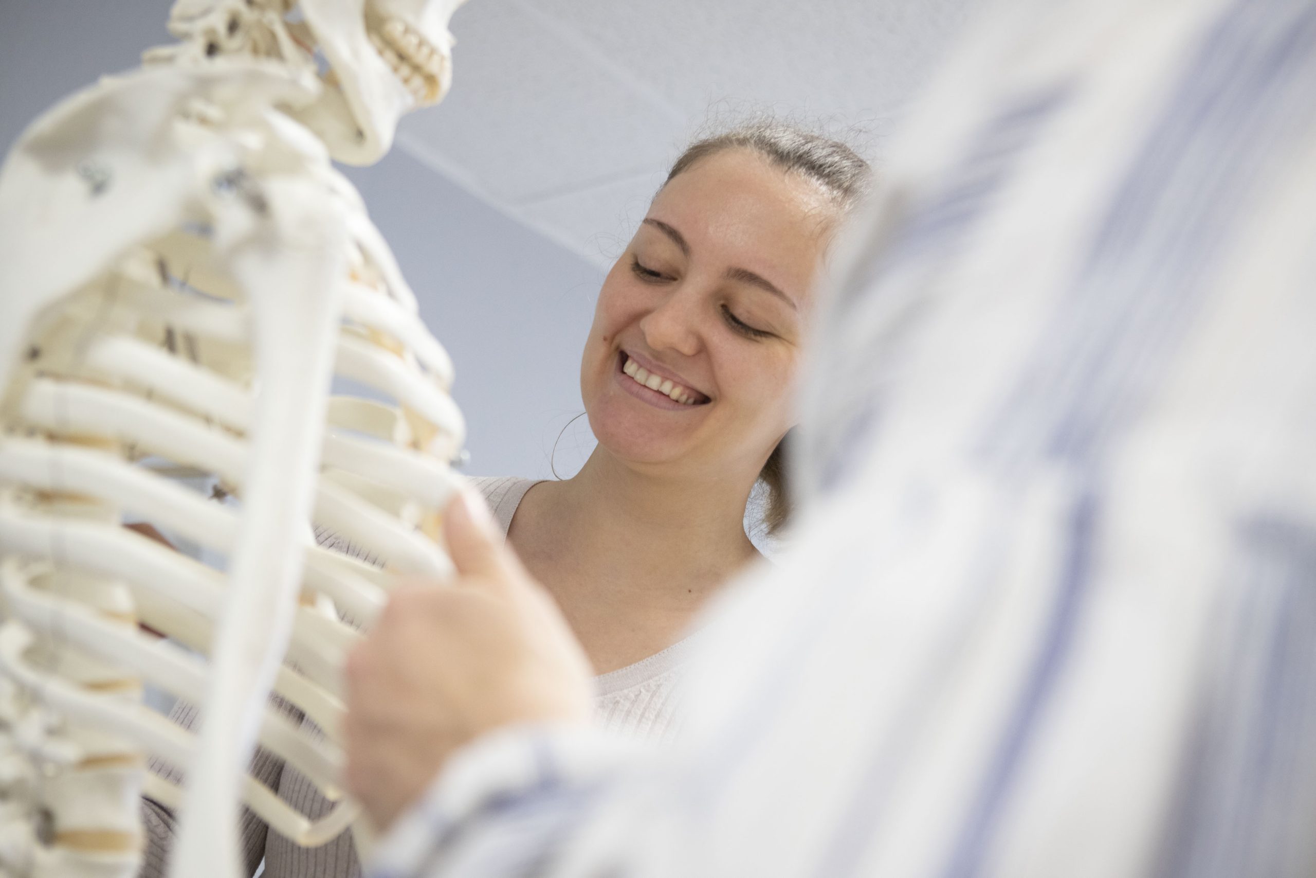 01A Lächelnder Student erhält Unterricht. Im Vordergrund steht das Skelettmodell.